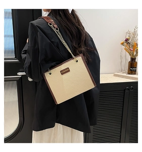 Détail d'un sac cabas en toile tissée avec garniture en cuir marron et chaîne dorée