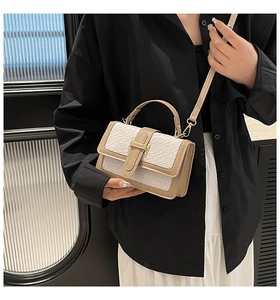 Detail of beige crocodile pattern handbag with gold clasp on model in black and white outfit
