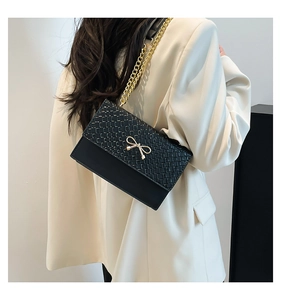 Detail of elegant black chain bag with golden bow buckle on off-white suit