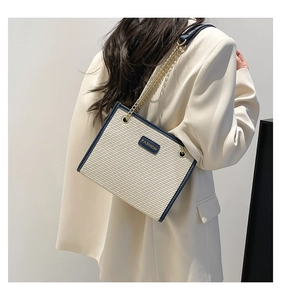 Gros plan du sac cabas tissé beige avec bordure en cuir bleu marine et chaîne dorée