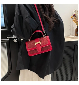 Red crossbody bag with woven flap and gold buckle worn by a model in a black shirt