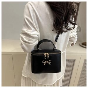 Fashionable black box bag with golden bow detail shown on a model in a minimalist setting