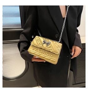 Detailed close-up of a metallic gold crossbody bag with fashion lettering and butterfly buckle