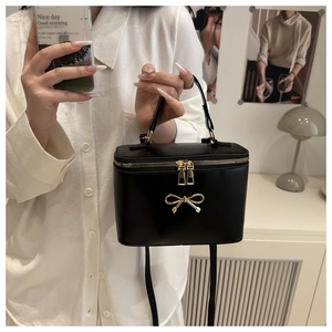 Detail of black box crossbody bag featuring a golden metal bow and dual zipper closures