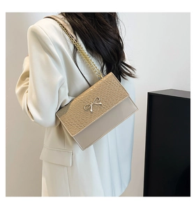 Detail of beige faux crocodile bag with golden bow and metal chain strap on model