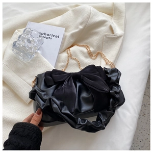Detail of black leather handbag with silk bow, golden chain strap on beige fabric