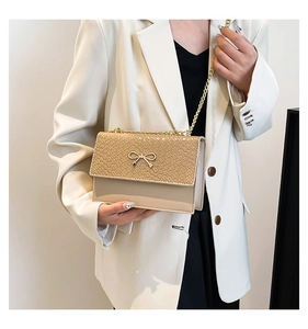 Detail of beige shoulder bag with stone texture, bow metal buckle, and chain strap