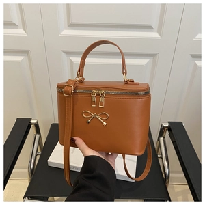 Detail of tan PU leather box bag featuring a golden bow and sleek metal zipper closure