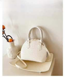 Detail of white crocodile texture shell handbag with golden hardware on display tray