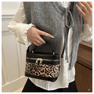 Close-up of a box-shaped handbag featuring leopard print patchwork and gold zippers