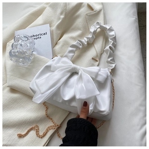 Detailed view of white satin handbag with oversized bow and golden chain strap