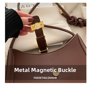 Dettaglio della chiusura magnetica dorata su una borsa a tracolla in pelle liscia marrone