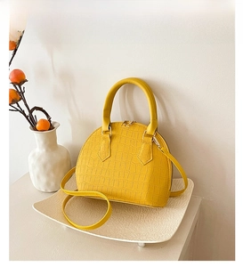 Detail of yellow shell handbag with crocodile pattern on white tray and elegant background