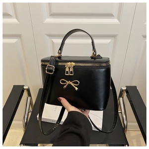 Detail of black leather box bag featuring golden bow accent and dual zipper closure