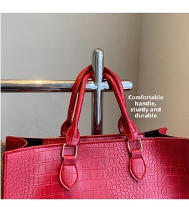 Detail of red crocodile texture handbag with silver rings and sturdy handle parts