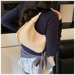Detail of beige woven hobo bag with gold metal chain strap shown on a shoulder