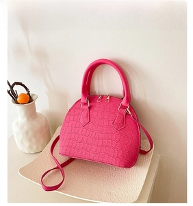 Detail view of rose red shell bag featuring crocodile pattern texture and golden zipper