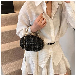 Detail of black tweed shell bag with gold metal handle and elegant chain strap