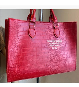 Detail of red crocodile pattern tote bag featuring double handles and gold metal rings
