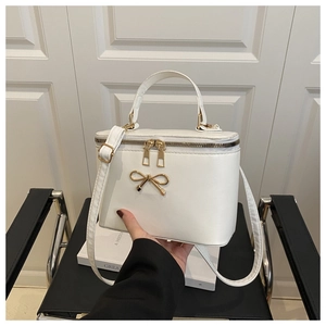 Detail of white box handbag featuring gold bow clasp and adjustable crossbody strap