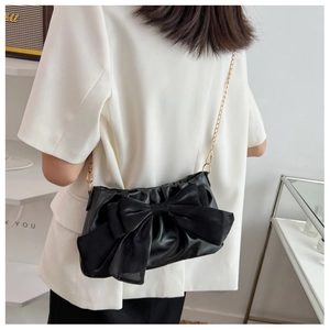 Detail of elegant black shoulder bag with a large bow and gold chain on a model