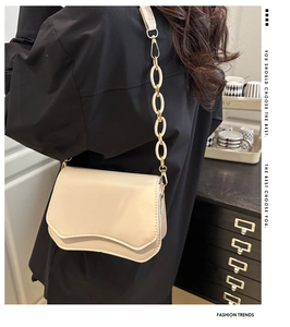 Detail of cream crossbody bag featuring a wavy flap and resin chain strap on model