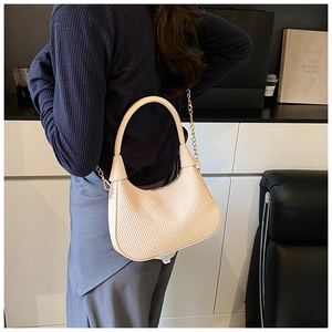 Detail of cream woven shoulder bag with gold chain strap on model's shoulder