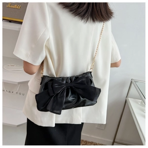 Detail of black cloud bag with oversized silk bow and elegant gold chain strap