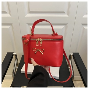 Macro detail of red box crossbody bag with golden bow hardware and adjustable strap