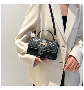 Detail of black woven crossbody bag with gold H-buckle on a stylish white blazer
