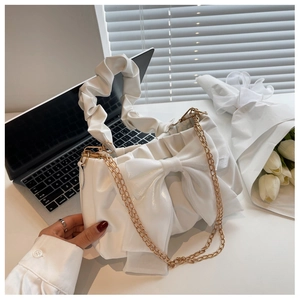 White ruched handbag with large bow and gold chain strap shown with lifestyle props