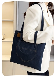 Detail of dark blue denim tote bag with contrast stitching and front pocket on white blazer
