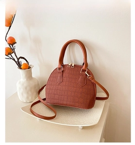 Detail of a brown crocodile pattern shell bag with golden zipper and metal feet