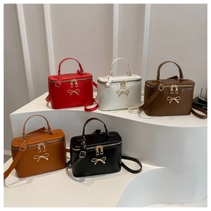 Five colored PU leather box bags with metal bow accent and top handles displayed on a white stand
