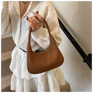 Close-up of brown woven texture and knot detail on a minimalist half-moon underarm bag