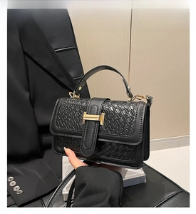 Close-up of black woven leather handbag with a prominent golden H-shaped metal buckle detail