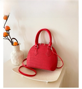 Detail shot of red crocodile texture shell handbag with gold hardware on a tray