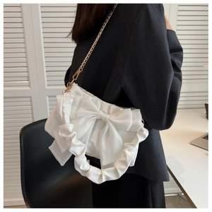 Detail of white handbag featuring a large bow and ruffled handle with a gold chain strap