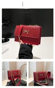 Detail of red crocodile texture handbag with gold bow clasp and metallic chain strap