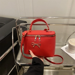 Elegant red leather handbag with gold bow clasp and adjustable shoulder strap