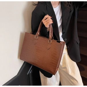 Brown crocodile embossed tote bag styled with a professional black suit on stairs
