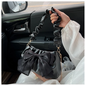 Detail of black faux leather handbag with oversized satin bow and gold chain strap