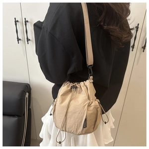 Detail of beige drawstring bucket bag featuring side mesh pocket and fashion label