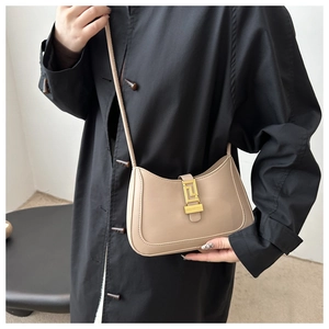 Dettaglio della borsa a tracolla in pelle beige con chiusura dorata su trench nero