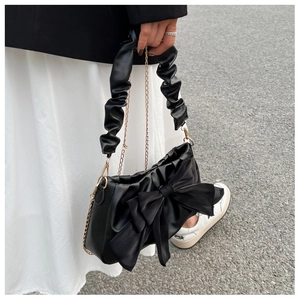 Detail of a black chic handbag featuring a large satin bow and ruched handle