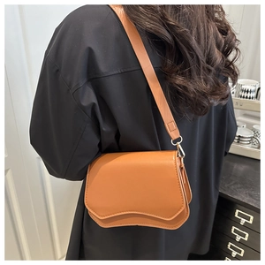 Detail of caramel faux leather crossbody bag featuring unique wave-shaped flap design