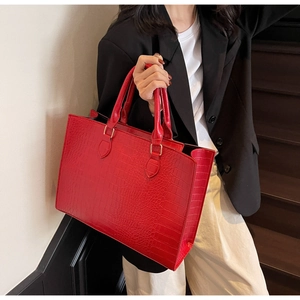 Detail of red crocodile pattern tote bag held by model in black suit for business look