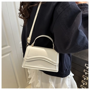 Détail du sac à main blanc avec rabat à vagues et boucle en métal doré sur la bandoulière