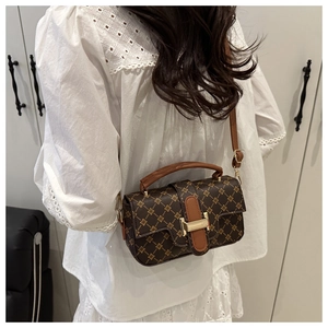 Brown handbag with vintage gold geometric pattern worn by a model in a white dress