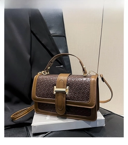 Close-up of brown straw woven bag with rectangular metal buckle on a stand